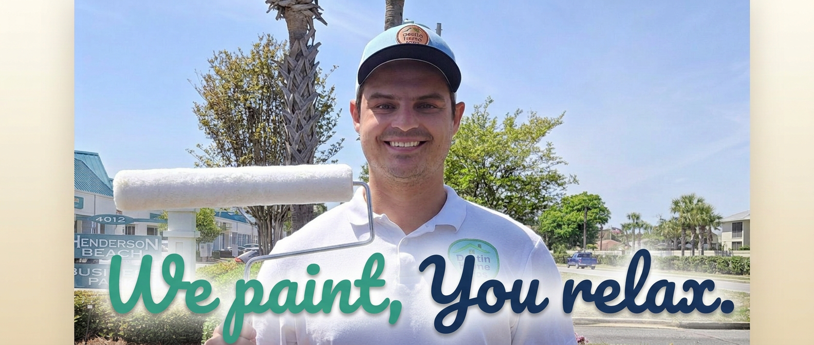 Nick Zellmer, owner of Destin Home Pros, holding a paint roller in front of the Henderson Beach Business Park sign with We Paint, You Relax on the sign